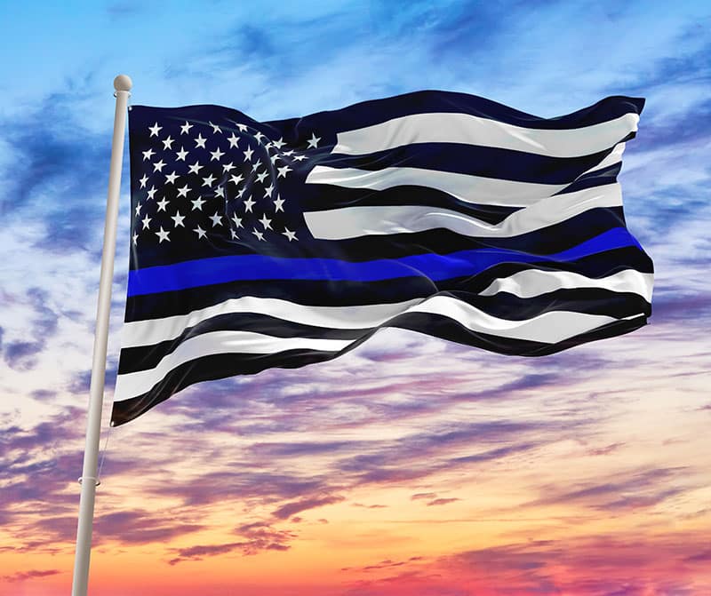 Black Flag of USA with Police Blue Line waving in the wind on flagpole against the sky with clouds on sunny day